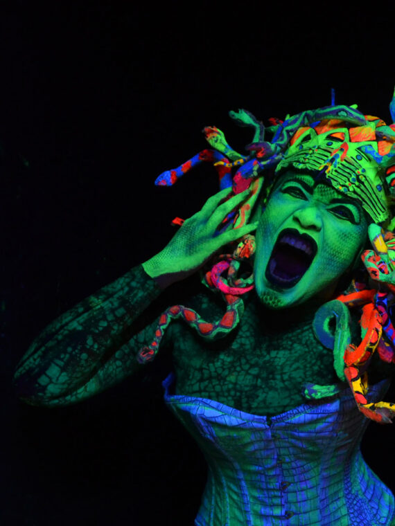 An actor with Halloween NIghts at Eastern State Penitentiary screams while wearing colorful clothing and snakes on her head