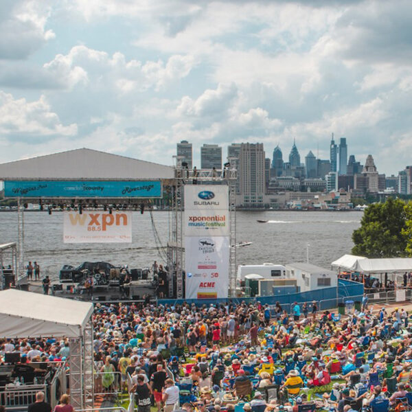 Una multitud al aire libre observa a los artistas con el río Delaware y el horizonte de Philly como telón de fondo en el Festival de Música XPoNential
