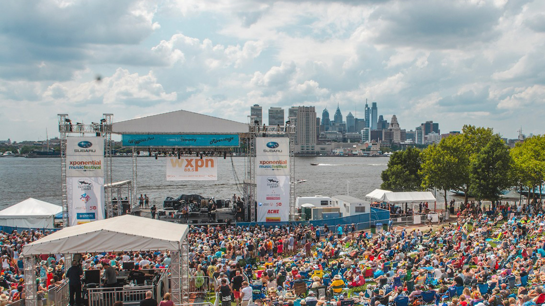 Au festival de musique XPoNential, une foule rassemblée en plein air admire les artistes, avec la rivière Delaware et la ligne d'horizon Philly en arrière-plan.