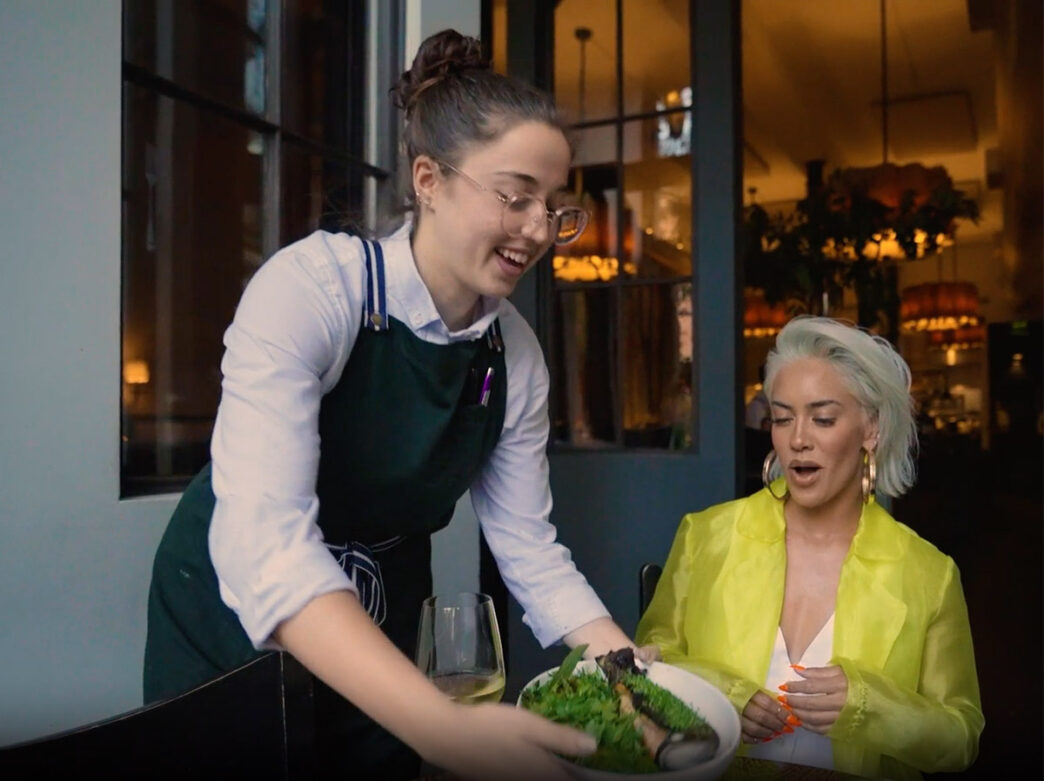 A waitress put food on the table in front of Sibley Scoles at Fork during a filming of 1st Look in Philadelphia