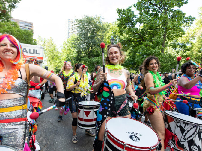 People marching and drumming in a parade for Pride and OURfest