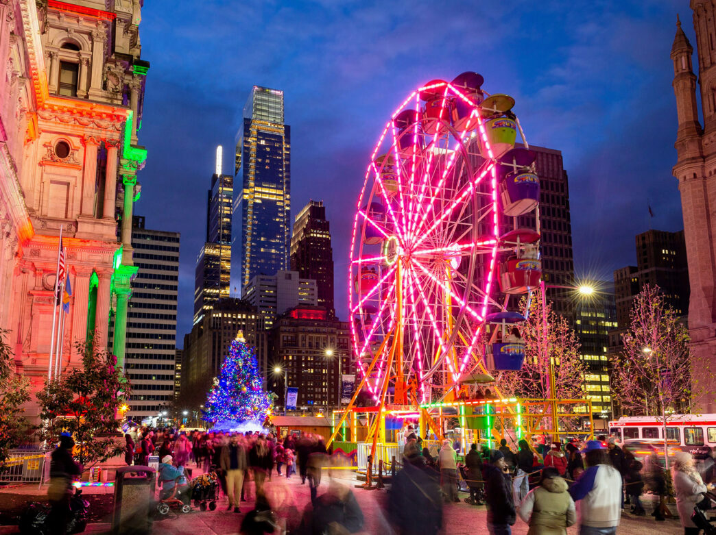 Crowds gather outside City Hall near a Ferris wheel and holiday tree during Christmas Village in Philadelphia