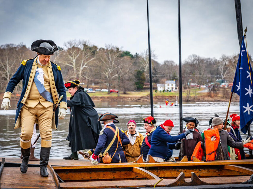 Des reconstituteurs historiques en costume colonial, dont l'un est déguisé en général George Washington, montent à bord d'une réplique de bateau sur le fleuve Delaware.