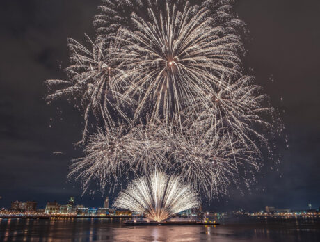 White and gold fireworks explode in the night sky over the Delaware River.