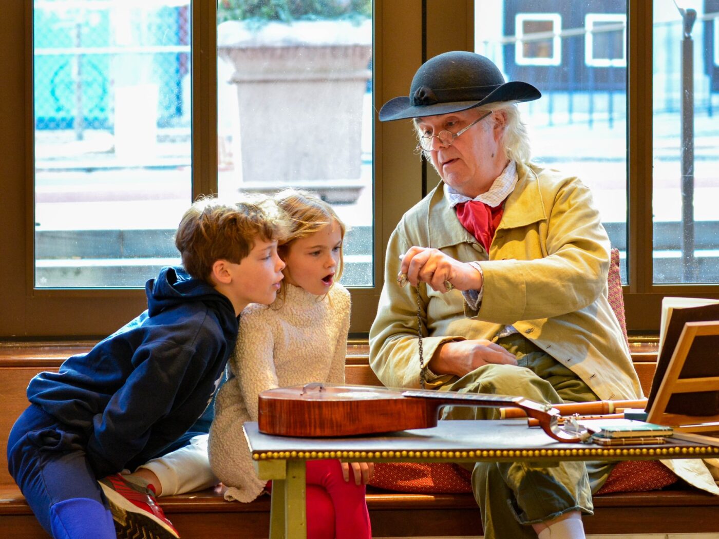 A man dressed in colonial garb shows 18th-century instruments to two children at the Museum of the American Revolution.
