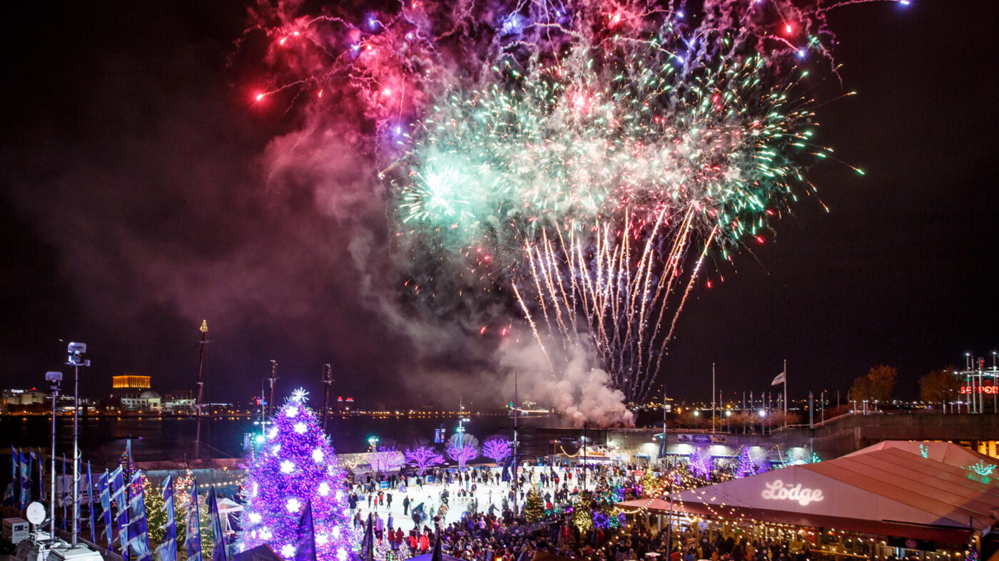 A wide-angle shot of people at Independence Blue Cross RiverRInk Winterfest watching the fireworks over the Delaware River in Philadelphia