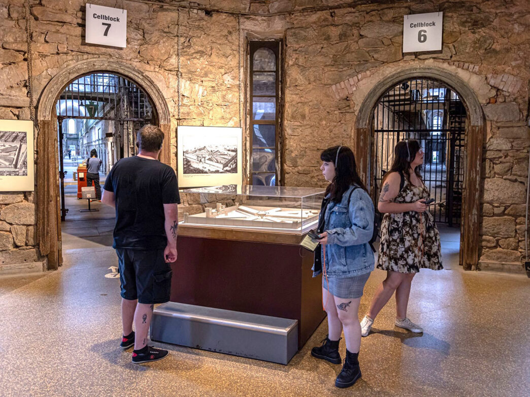 Three college students wearing headphones in front of Cellblocks 6 and 7 for audio tour at Eastern State Penitentiary.