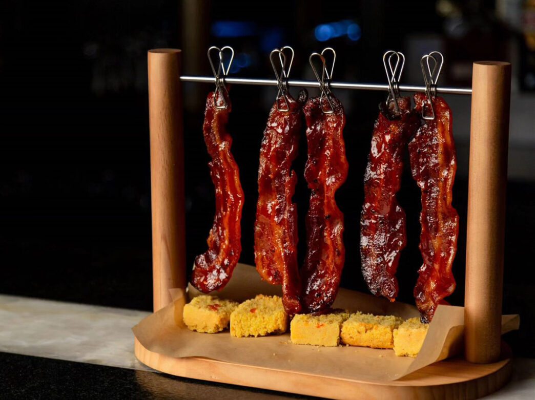 Strips of cooked bacon are hung artfully above pieces of bread.