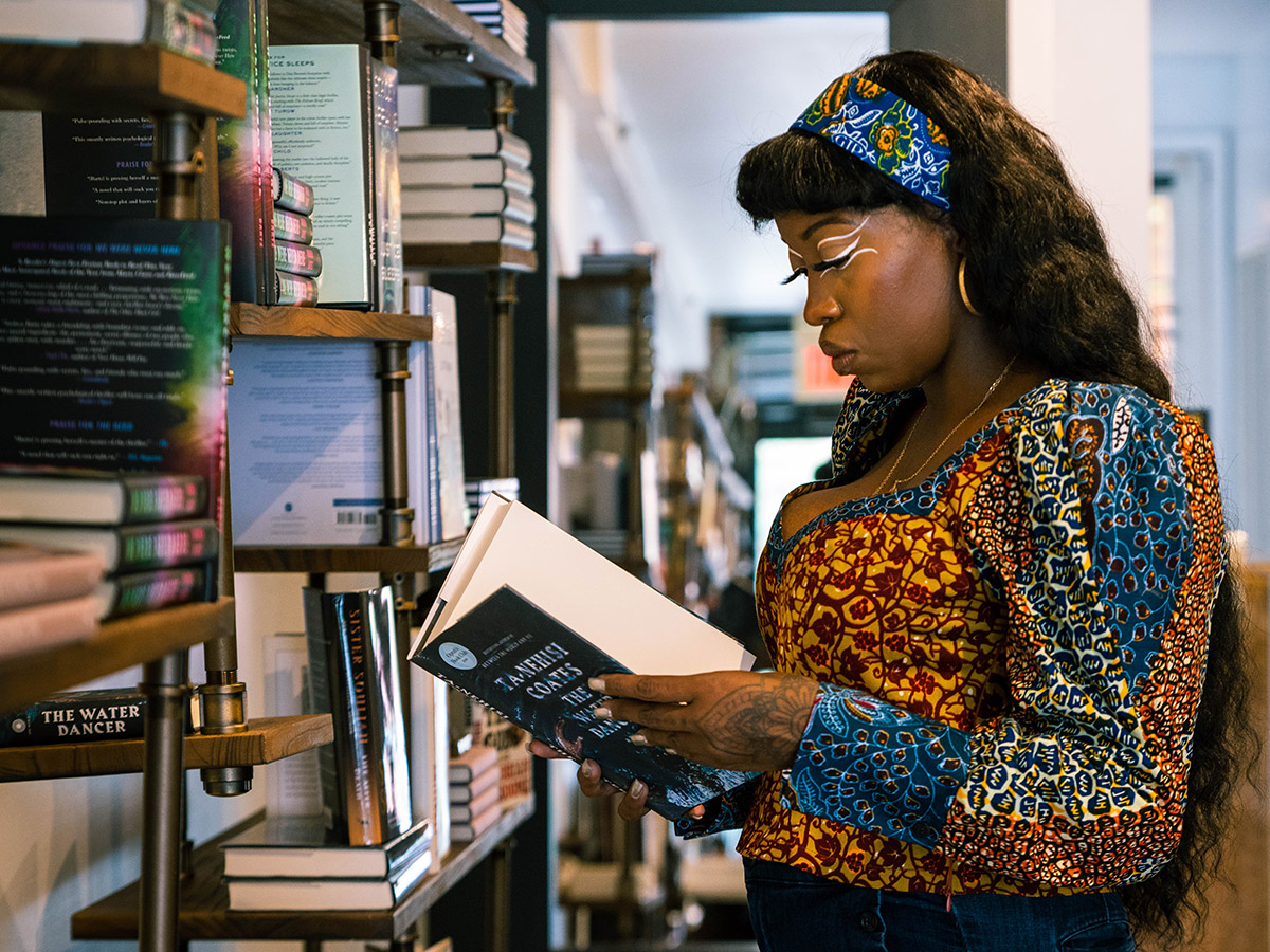 A woman in a colorful shirt and matching headband reads the inside cover of a book from the bookshelf at Harriett's Bookshop in Philadelphia.