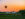 Rainbow hot air balloon floats over farm at sunset with barns and cows in the field.