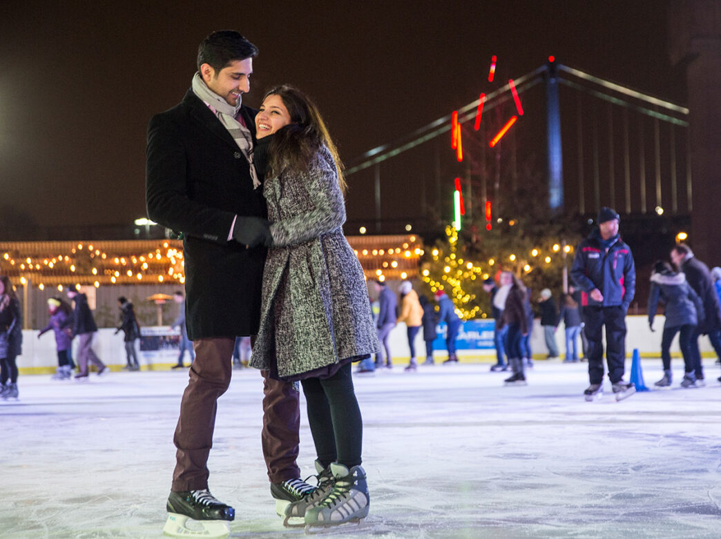A couple smiles and embraces one another while ice skating at the Independence Blue Cross RiverRink.
