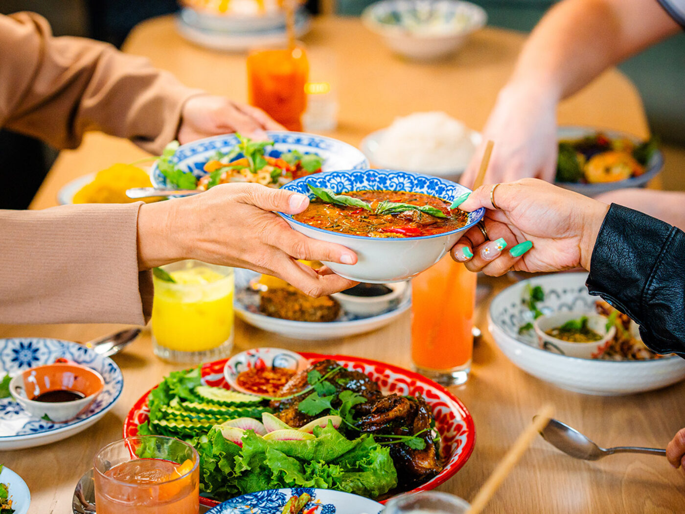 Various Thai dishes and meals spread across at table at Kalaya with diners sharing and passing a dish from one to another.