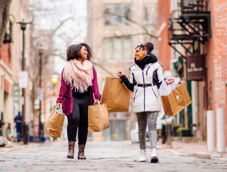 Two women walk down cobblestone street in Old City Philadelphia with several shopping bags in hand.