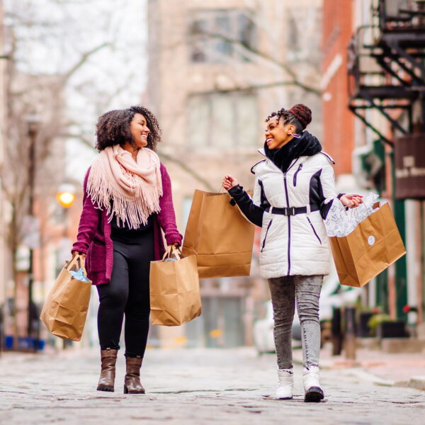 Two women walk down cobblestone street in Old City Philadelphia with several shopping bags in hand.