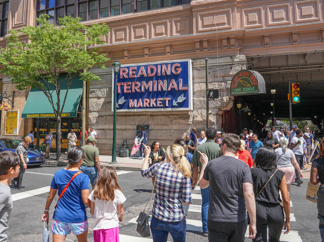 Exterior of Reading Terminal Market with crowds crossing 12th Street.