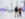 Two men wearing winter jackets smiling, holding hands, and skating across the ice skating rink at Independence Blue Cross RiverRink Winterfest. Trees with twinkling lights and the Benjamin Franklin bridge can be seen in the background behind the couple.
