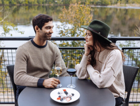 Couple drinking wine at a round table on the deck at River House at Odette's. View is overlooking Delaware River during fall.