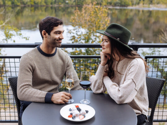 Couple drinking wine at a round table on the deck at River House at Odette's. View is overlooking Delaware River during fall.