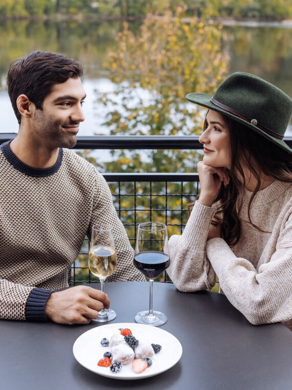Couple drinking wine at a round table on the deck at River House at Odette's. View is overlooking Delaware River during fall.