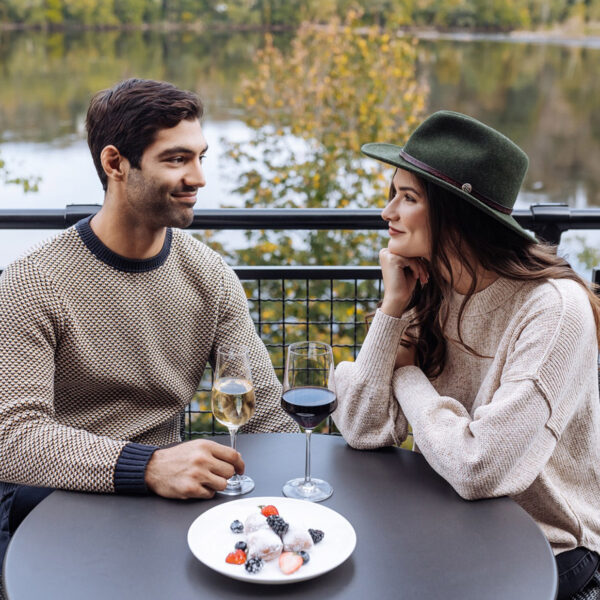 Couple drinking wine at a round table on the deck at River House at Odette's. View is overlooking Delaware River during fall.