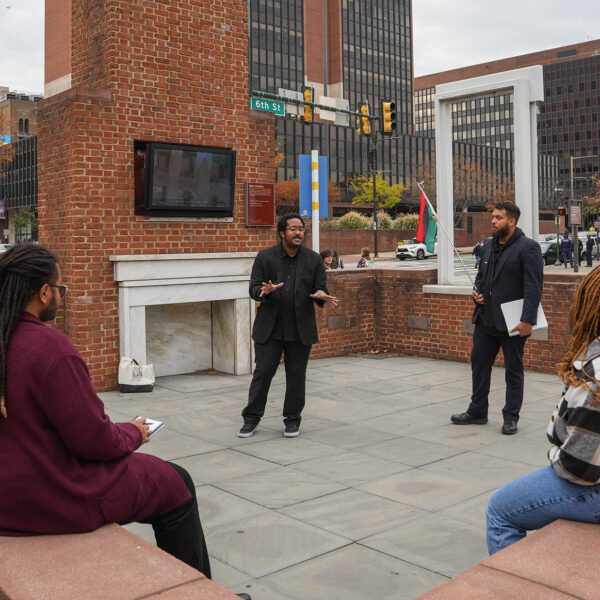 A tour guide from The Black Journey speaks to a group of seated tourgoers at The President's House in Philadelphia