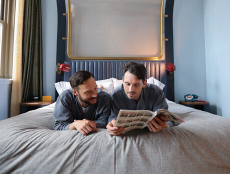 Una pareja está tumbada en la cama boca abajo leyendo juntos una revista en el Canopy by Hilton Philadelphia Center City.
