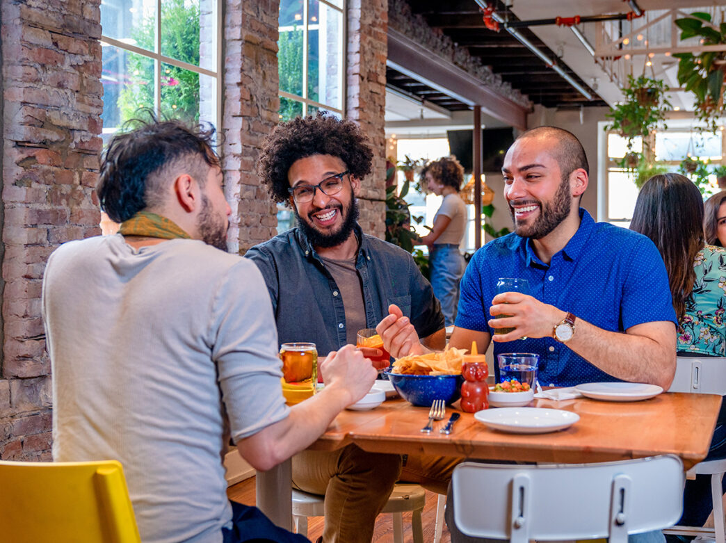 Three people dine at Mission Taqueria. On the table, there are chips, salsa and drinks.