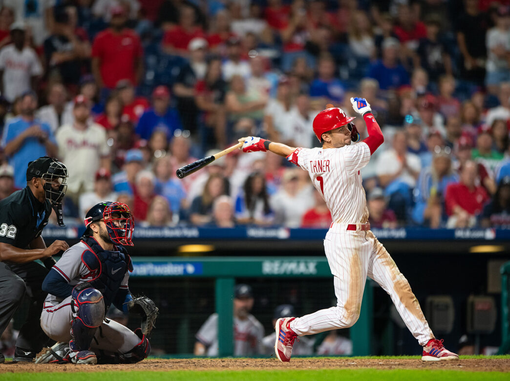 Trea Turner of Philadelphia Phillies swings baseball bat in front of catcher and umpire.