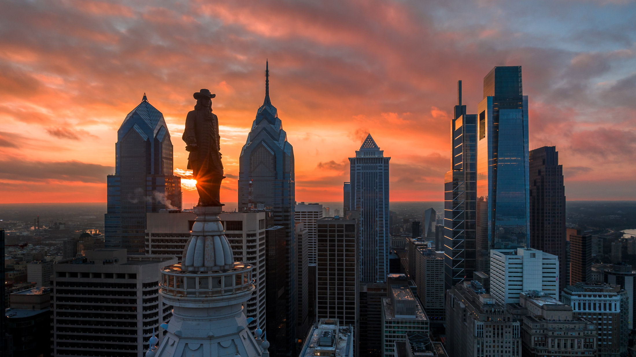 The William Penn statue atop City Hall and the Philadelphia skyline at sunset.
