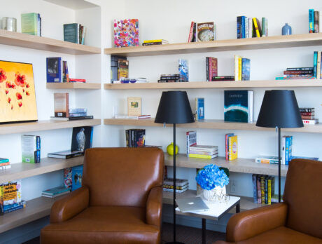 A modern hotel room with colorful books lining the shelves and brown leather chairs in the foreground