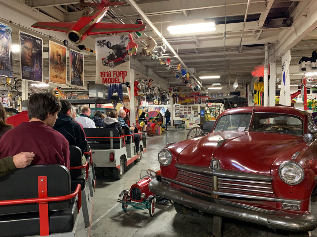 Visitors ride a trolley past a vintage red car in the American Treasure Tour Museum in Oaks, PA.