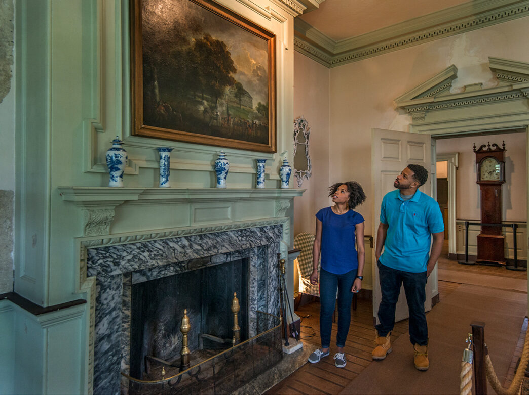 Two people look at a painting displayed over a fire place at Cliveden in Philadelphia.