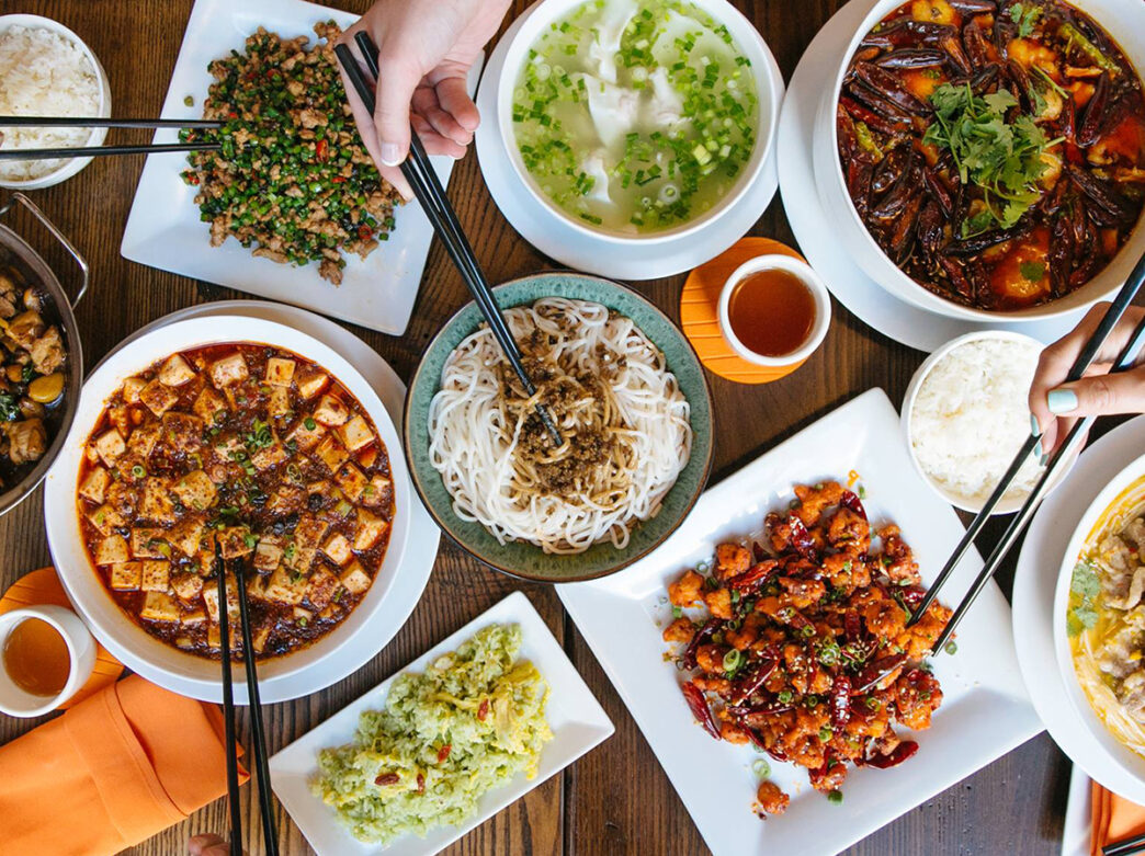 An overhead shot of diners with chopsticks reaching to grab different food items displayed on the table at DanDan.