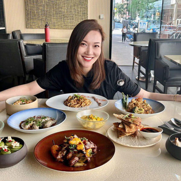 Chef Sally Song of Dim Sum Garden smiles for the camera while sitting behind a table of menu items.