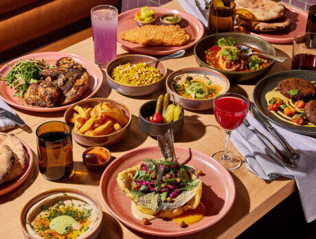 A table is set with various menu items including hummus, pita, roast chicken, rice pilaf, chicken schnitzel, dorade and more at Dizengoff in Philadelphia.