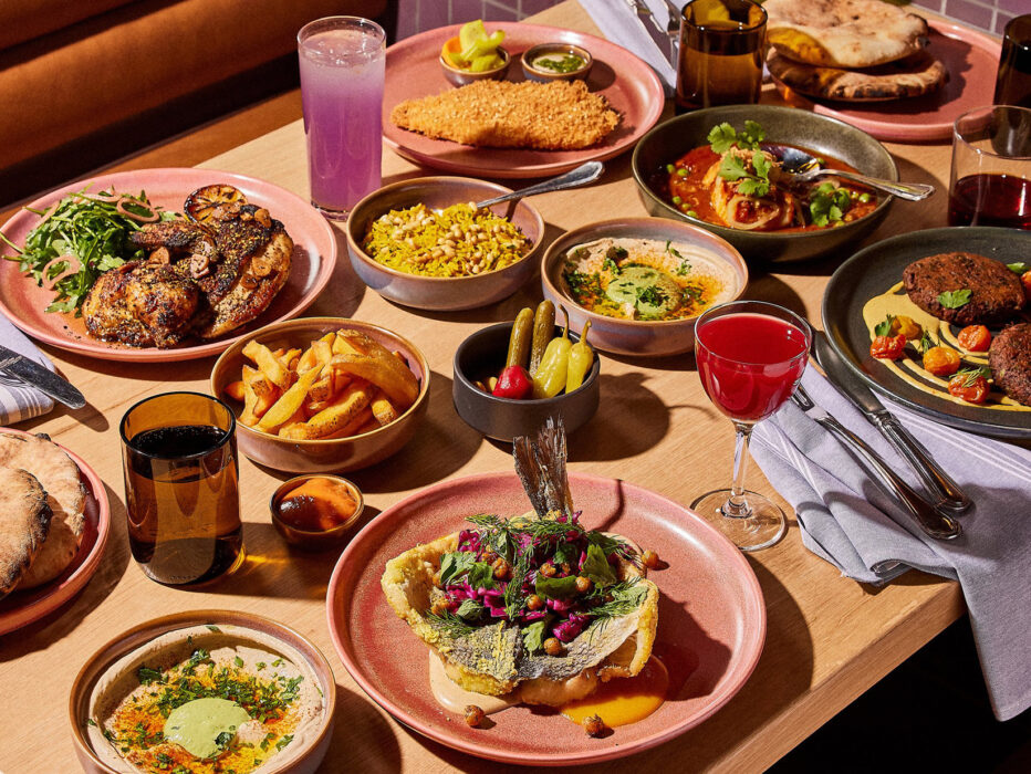 Uma mesa com vários itens do cardápio, incluindo homus, pita, frango assado, arroz pilaf, schnitzel de frango, dorade e muito mais no Dizengoff, na Filadélfia.