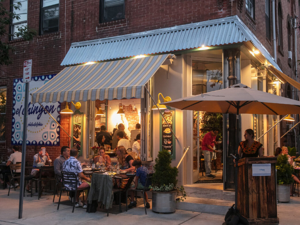The exterior of El Chingon in Philadelphia with people dining outdoors and the hostess stand.