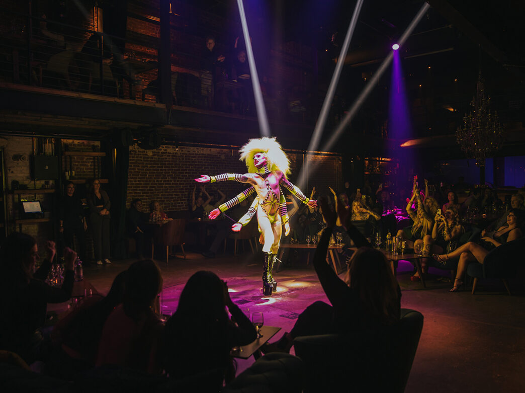A drag performer wearing a costume with extra arms performs at Fabrika in Philadelphia while the crowd cheers on.