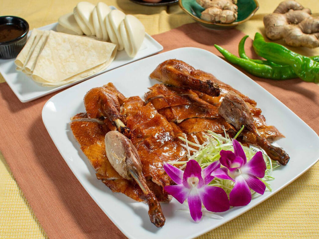A dish of Peking duck is displayed on a table with bright edible flowers at Sang Kee Peking Duck House in Philadelphia.
