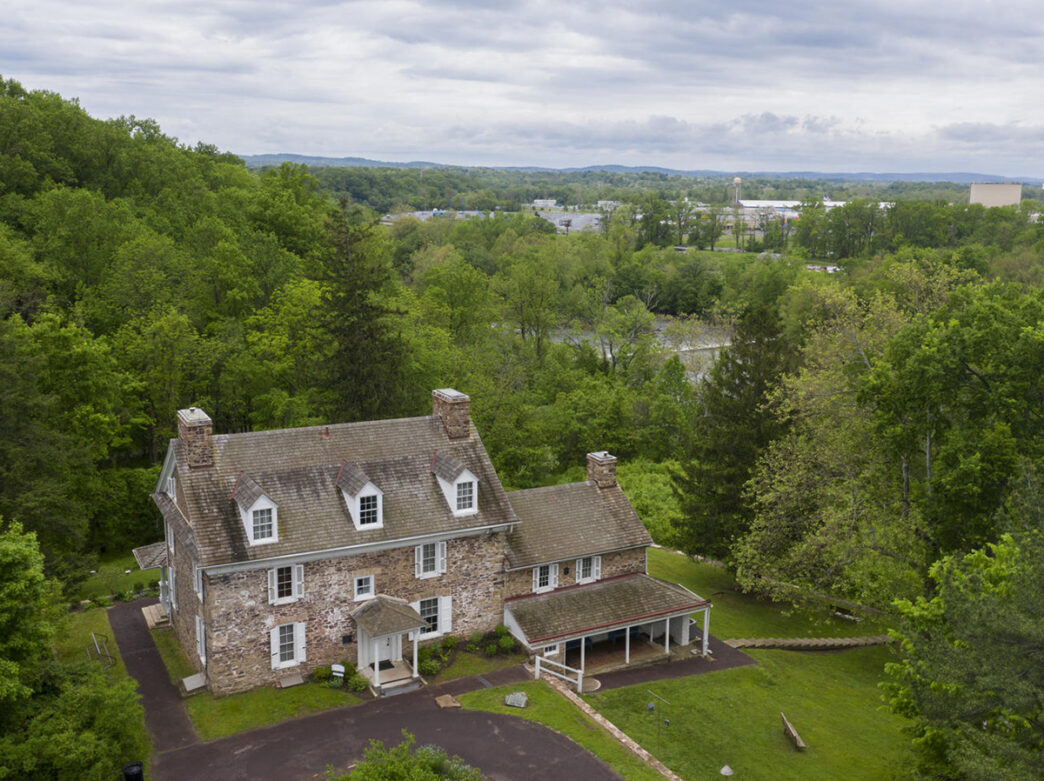 Una vista aérea tomada con un dron de la Casa Histórica, rodeada de árboles frondosos, en el Centro John James Audubon de Mill Grove.