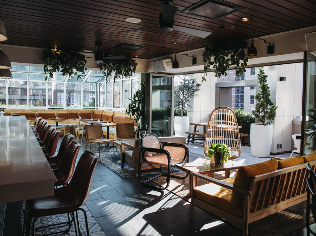 Bar and seating areas with plants hanging from the ceiling and a large slider door open to the rooftop at Attico Rooftop Lounge.
