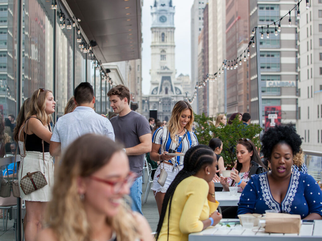 People socialize on the Balcony Bar at the Kimmel Center overlooking Broad Street with City Hall in the background.