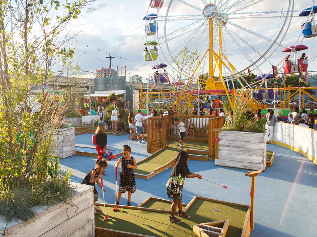 Kids play mini-golf with a Ferris wheel in the background at the Blue Cross RiverRink Summerfest in Philadelphia.