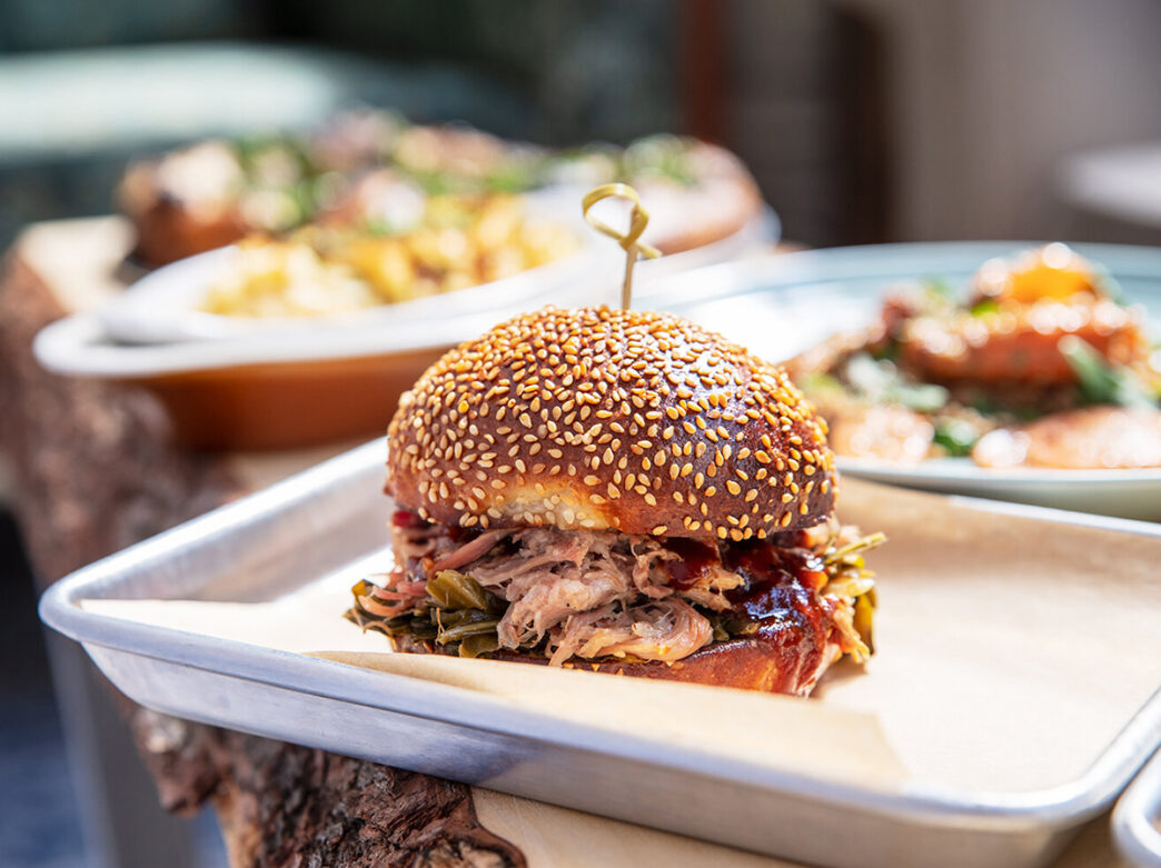 Pulled pork on a seeded bun with a toothpick through the center is displayed on a metal food tray at Craft Hall.
