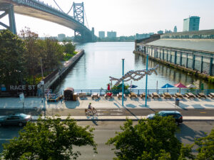 Een fietser met een helm rijdt langs de Delaware River Trail voor de Race Street Pier, Cherry Street Pier en Benjamin Franklin Bridge.