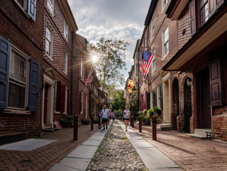 Mensen lopen over de geplaveide straten van Elfreth's Alley in Philadelphia terwijl de zon achter een huis opkomt.