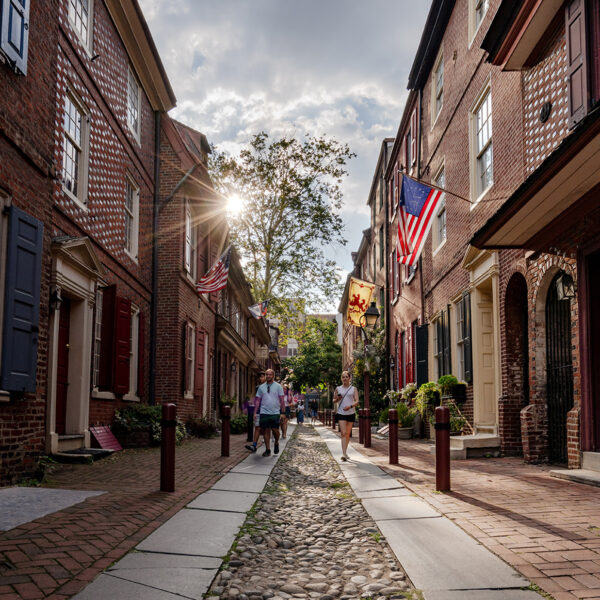 Des personnes marchent dans les rues pavées d'Elfreth's Alley, à Philadelphie, alors que le soleil se lève derrière une maison.