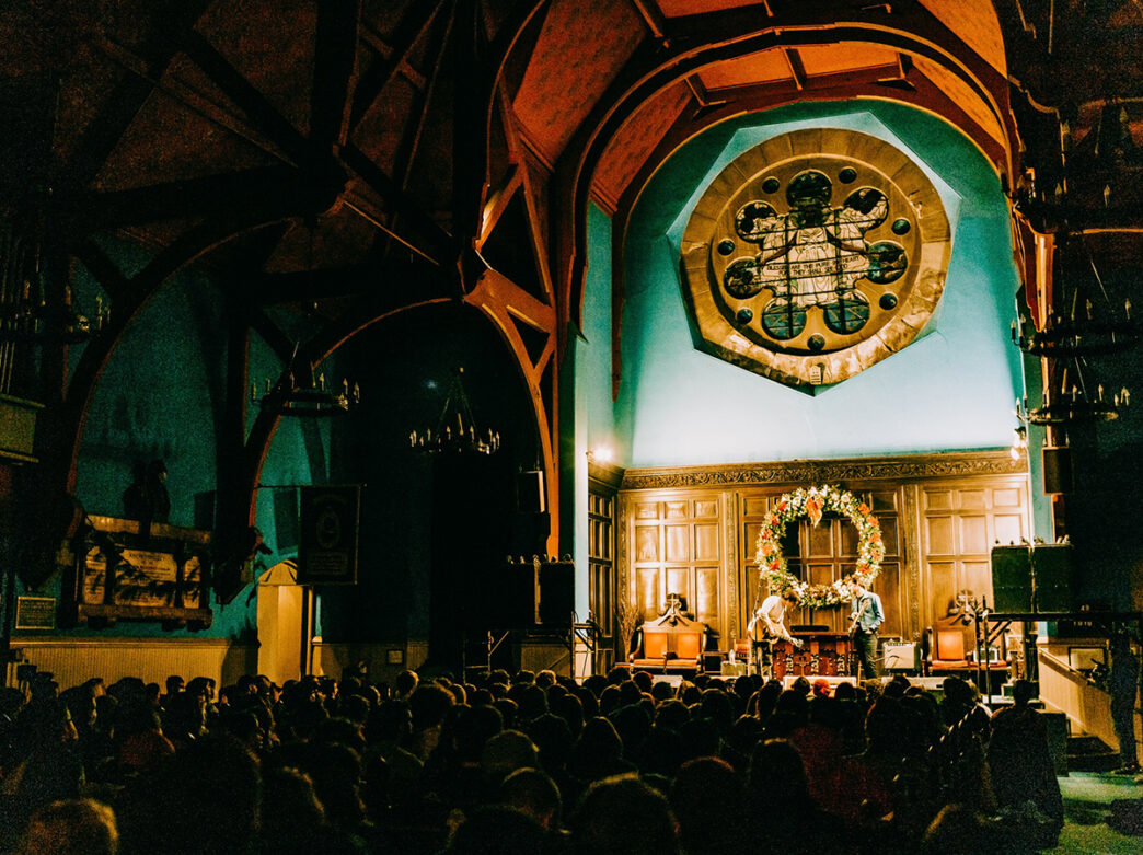 Musicians perform on stage at First Unitarian Church of Philadelphia while a crowd is seated in the pews.