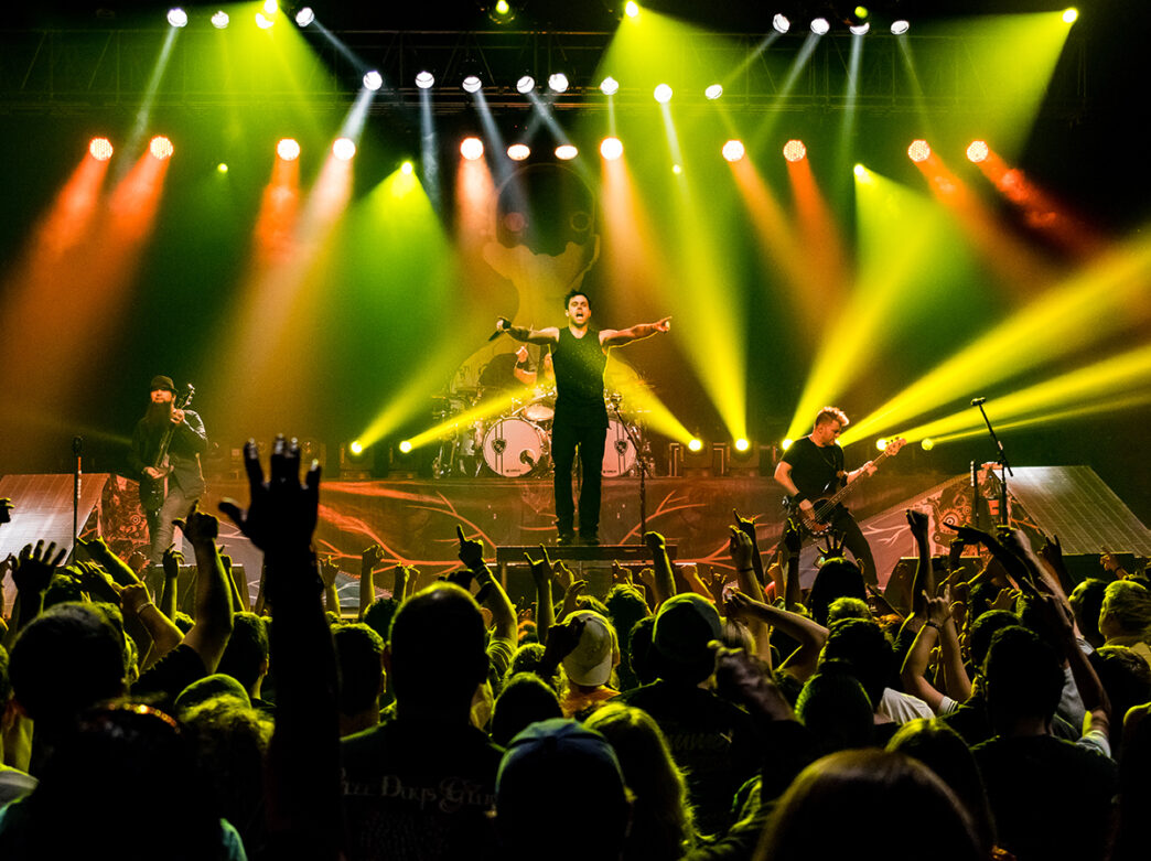 A band performs on stage at Franklin Music Hall with red and green stage lights while the crowd on the floor cheers the band on.