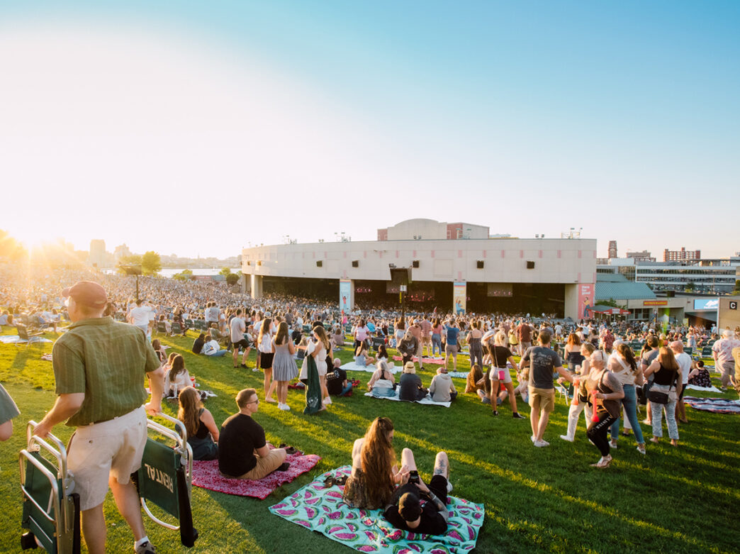 Concert attendees lay on blankets and walk around on the lawn in front of the stage at Freedom Mortgage Pavilion.